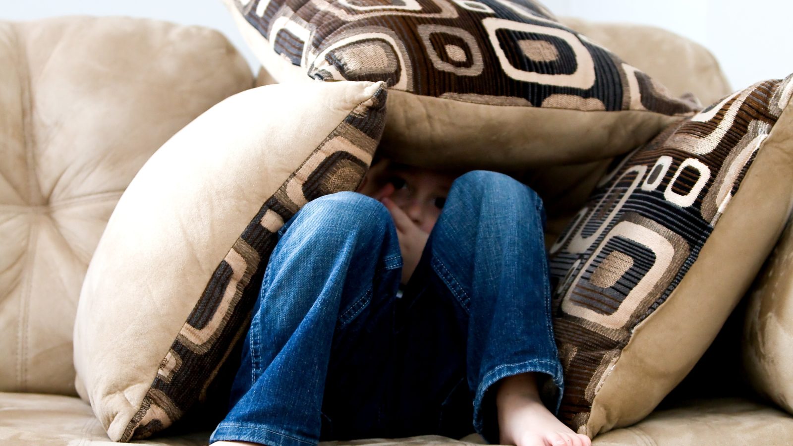 Child hiding under pillows representing parental alienation during a high-conflict divorce or separation