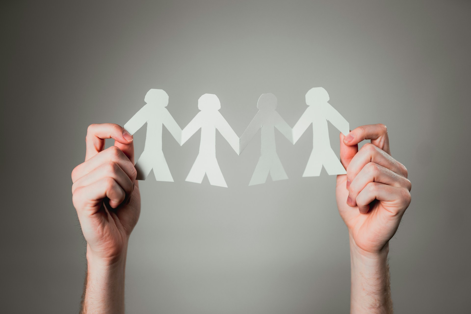 Two hands hold up four paper dolls connected by the hands, representing family trusts and divorce.